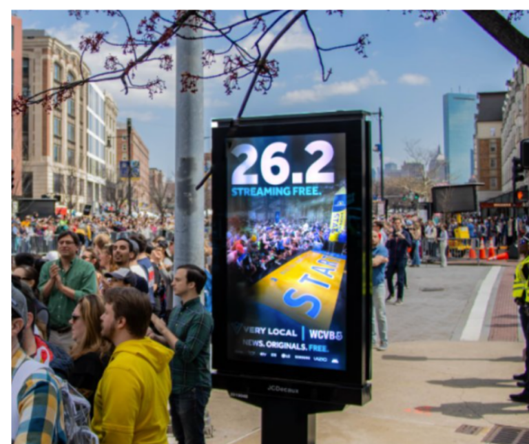 Digital advertising panel next to a race route, featuring a campaign for Very Local, reaching participants and spectators as part of an out-of-home media strategy.